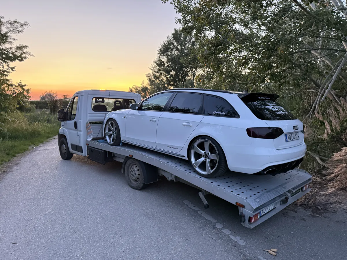 Fehér Audi kombi autószállítása platós autómentőn naplementében
